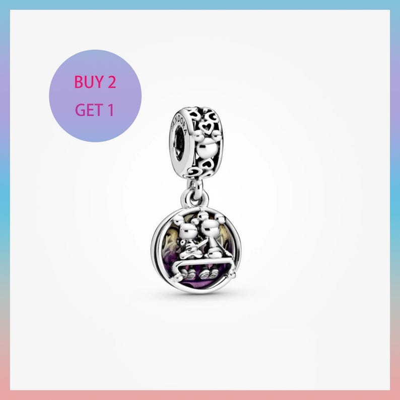 May include: A silver charm with a round pendant featuring two cartoon figures. The charm has a decorative top with heart and Mickey Mouse head cutouts. The pendant has a purple and yellow background. The text "BUY 2 GET 1" is in a purple circle.