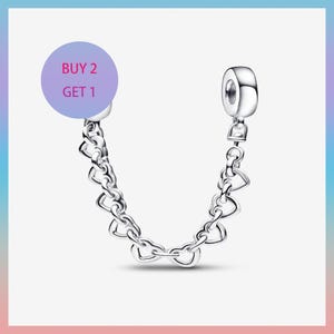 May include: A silver charm bracelet safety chain featuring heart-shaped links. The chain connects two ends, each with a cylindrical bead. A purple circle with the text "BUY 2 GET 1" is in the upper left corner.