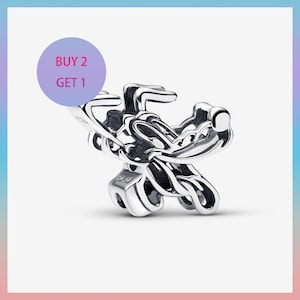 May include: A silver-colored charm with a stylized design. The charm has a complex, intertwined shape with rounded edges. A purple circle with the text "BUY 2 GET 1" is in the upper left corner.