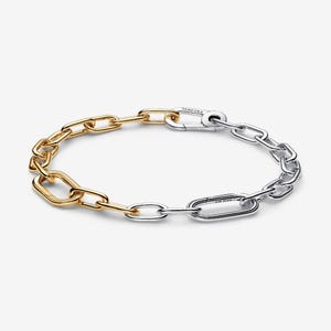 May include: A two-tone chain bracelet. One half is gold-colored, the other is silver-colored. The bracelet is made of interlocking oval and rectangular links. The clasp is silver-colored and has the brand name engraved on it.