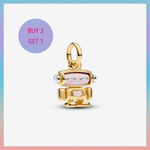 May include: A gold-colored robot charm with a pink face and a heart on its chest. The robot has silver accents on its head and arms. The charm is suspended from a gold loop. A purple circle with the text "BUY 2 GET 1" is in the background.