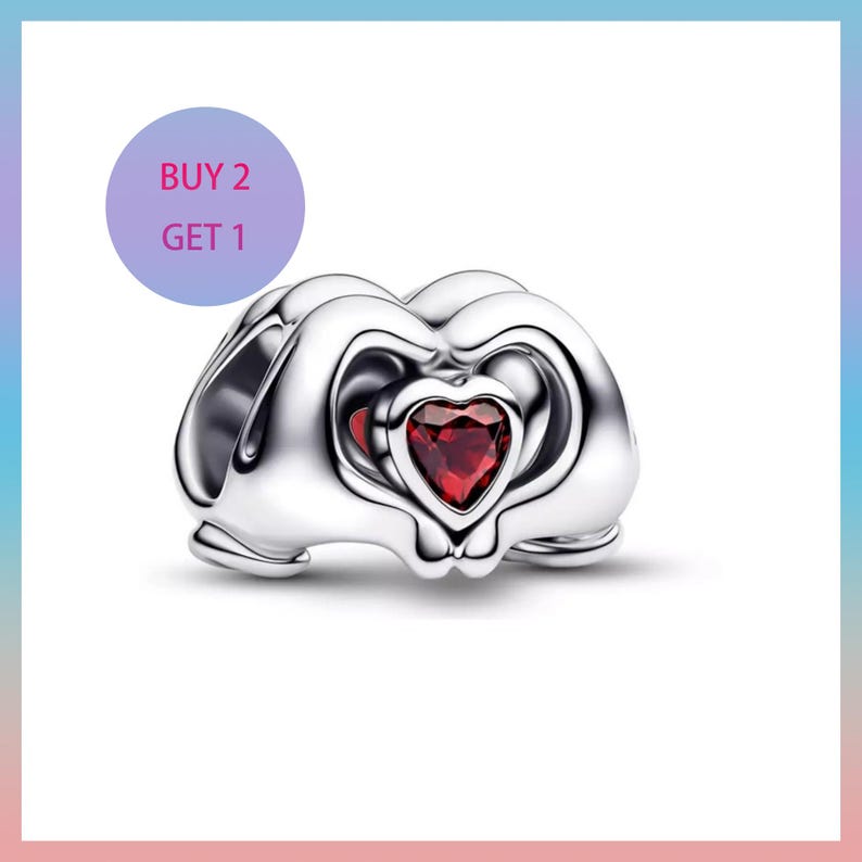 Puede incluir: Un charm de color plateado con un coraz&oacute;n rojo en el centro. El charm tiene un dise&ntilde;o &uacute;nico con elementos curvos y calados. Un c&iacute;rculo p&uacute;rpura con el texto "BUY 2 GET 1" est&aacute; en la esquina superior izquierda.
