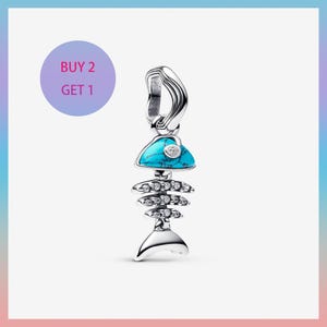 May include: A silver charm shaped like a fish skeleton, featuring a turquoise blue head with a small, clear gem. The charm has multiple clear gems along the spine and a tail fin. The text "BUY 2 GET 1" is in a purple circle.