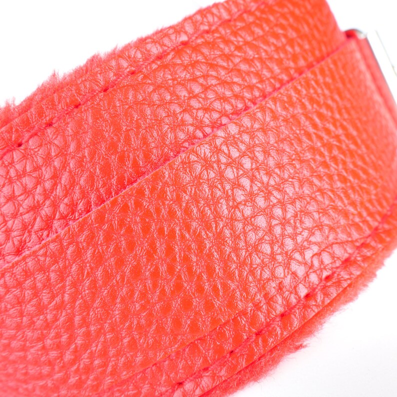 May include: Close-up of a vibrant red leather belt. The textured surface of the leather is visible, with detailed stitching along the edges. The belt appears to be new and unused, with a bright, saturated color.