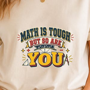 Könnte beinhalten: Ein cremefarbenes Kurzarm-T-Shirt mit einem Grafikdruck, der den Text "MATH IS TOUGH BUT SO ARE YOU" in Blau, Rot und Gelb zeigt. Das Design enthält mathematische Symbole wie ein Dreieck, einen Zirkel und die Gleichung a²+b²=c².