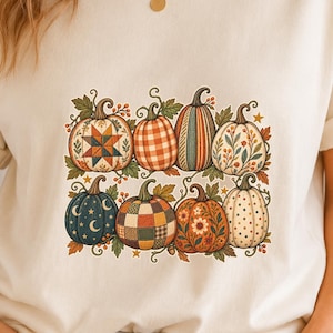Peut inclure: Un t-shirt à manches courtes de couleur crème avec une impression graphique de huit citrouilles disposées sur deux rangées. Les citrouilles présentent divers motifs dont des étoiles, des carreaux, des rayures, des fleurs et des pois.