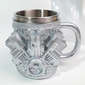 Puede incluir: Taza plateada con un diseño detallado de motor V6. La taza tiene un interior de acero inoxidable y un asa curvada. El diseño del bloque del motor presenta pistones y otros detalles mecánicos, lo que la convierte en un regalo único.