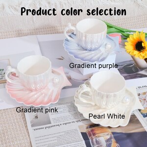 May include: A set of three ceramic teacups and saucers in gradient pink, gradient purple, and pearl white. Each cup has a pearl accent on the handle and sits on a seashell-shaped saucer. The text "Product color selection" is at the top.