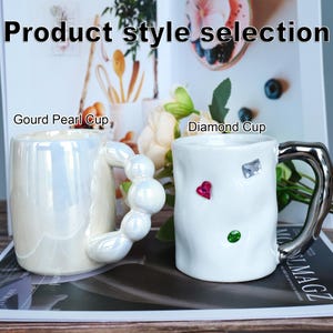 May include: Two ceramic mugs. One is pearlescent white with a handle of connected spheres, labeled "Gourd Pearl Cup." The other is white with a silver handle and gem-like embellishments, labeled "Diamond Cup." The text "Product style selection" is at the top.