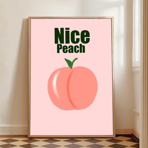 Könnte beinhalten: Gerahmter Kunstdruck mit einer Pfirsich-Illustration. Der Pfirsich ist zartrosa mit einem grünen Blatt, vor einem hellrosa Hintergrund. Die Worte "Nice Peach" stehen in Dunkelgrün oben auf dem Druck.