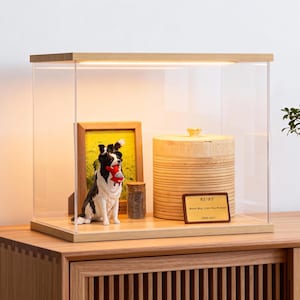 May include: A wooden display case with a clear acrylic front houses a framed photo, a dog figurine holding a red toy, a small jar, and a wooden container with a lid. A plaque reads "RUBY" and a message.