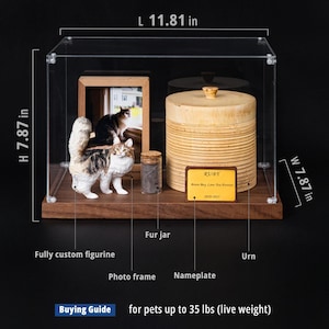 May include: A display case with a wooden base, containing a cat figurine, photo frame, fur jar, and urn. The urn has a nameplate that reads "RUBY". The case is 11.81 inches long, 7.87 inches high and 7.87 inches wide. The text "Buying Guide" is visible.
