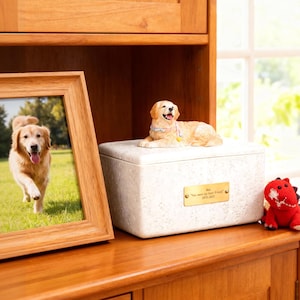 May include: A wooden framed photo of a Golden Retriever dog running on grass. A cream-colored pet urn with a dog figurine on top and a small red stuffed dinosaur are on a wooden shelf.
