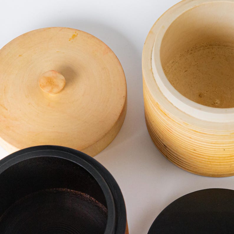 May include: Wooden storage containers with lids. One container is light brown with a matching lid and a small knob. Another container is a darker brown with a black lid. The third container is light brown with a white interior.