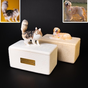 May include: Two pet urns, one with a cat figurine and the other with a dog figurine. The cat urn is white with a gold plaque that reads "You were my best friend". The dog urn is beige.