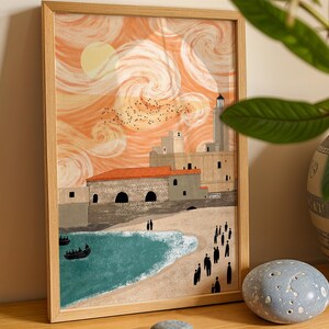 Peut inclure: Une impression d'art encadrée représentant une scène côtière avec un ciel tourbillonnant orange clair, un soleil jaune pâle et une volée d'oiseaux. Des bâtiments en pierre aux toits rouges bordent une plage de sable, une mer turquoise et des silhouettes.