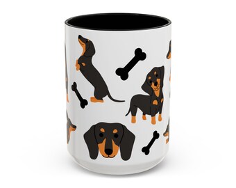 May include: White ceramic mug with a black interior, featuring a repeating pattern of black and tan dachshund dogs and black bone shapes. The mug is cylindrical and has a glossy finish.