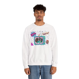 Op de afbeelding: Witte sweatshirt met een kleurrijk jaren 90 retro-ontwerp. De afbeelding bevat een turquoise televisie met een cartoonfiguur, de woorden "90's" en "Retro" en een geometrisch patroon. Unisex stijl.