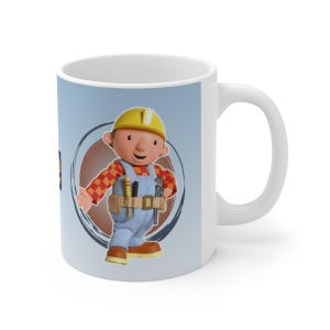 Peut inclure: Mug en céramique blanche avec un dessin de Bob le Bricoleur, portant un casque jaune et une salopette bleue. Le personnage est placé sur un fond bleu clair avec un cercle marron et des coups de pinceau bleu foncé.