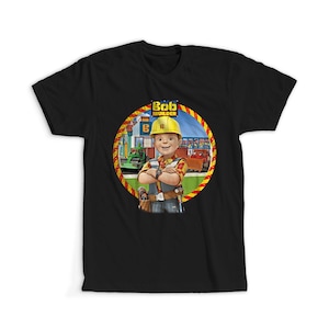 Peut inclure: T-shirt noir avec un motif circulaire de Bob le Bricoleur, un personnage de dessin animé portant un casque jaune et des vêtements de travail. Le motif comprend les mots "Bob le Bricoleur".