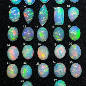May include: A collection of 27 opals, each with unique shapes and iridescent color patterns. The opals vary in size and shape, with oval, teardrop, and rectangular forms. The colors include blues, greens, oranges, and pinks, creating a vibrant display.