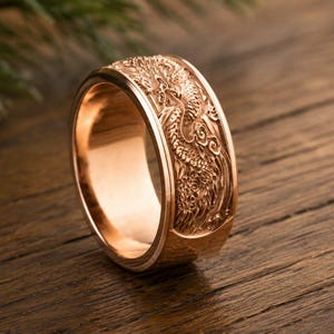 Pu&ograve; includere: Un anello color oro rosa caratterizzato da un dettagliato design a drago in rilievo che avvolge la fascia esterna. L'anello presenta una superficie interna liscia e lucida e un profilo largo e piatto con intricati rilievi del drago.