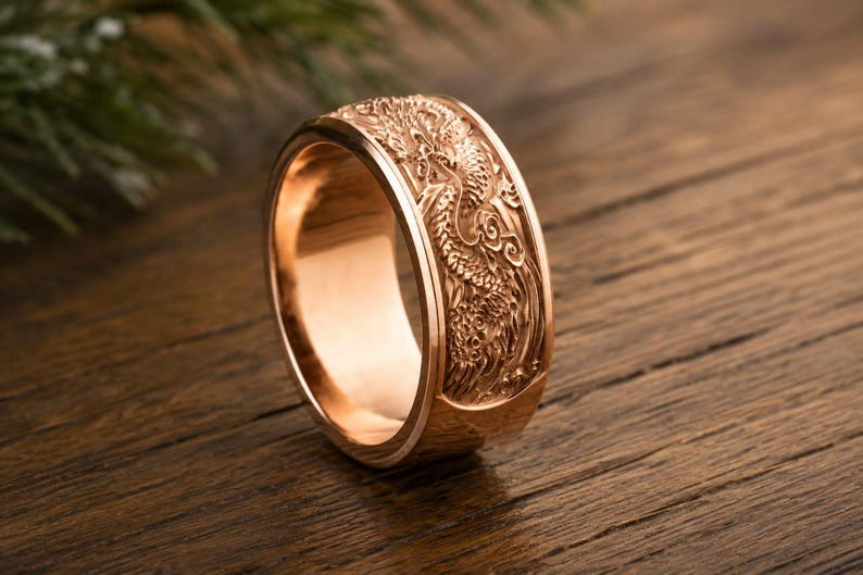 Pu&ograve; includere: Un anello color oro rosa caratterizzato da un dettagliato design a drago in rilievo che avvolge la fascia esterna. L'anello presenta una superficie interna liscia e lucida e un profilo largo e piatto con intricati rilievi del drago.