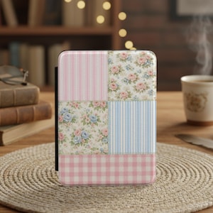 Op de afbeelding: Een decoratieve hoes met een patchwork ontwerp. De hoes heeft vierkanten met roze strepen, bloempatronen en blauwe strepen, met een roze ruitjespatroon aan de onderkant. De hoes staat op een houten tafel met een geweven placemat.