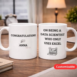 Könnte beinhalten: Zwei weiße Keramikbecher mit schwarzem Text. Auf einem Becher steht "HERZLICHEN GLÜCKWUNSCH ANNA Ctrl+X" mit einer festlichen Grafik. Auf dem anderen Becher steht "ÜBER EINEN DATENWISSENSCHAFTLER ZU SEIN, DER NUR EXCEL VERWENDET" mit einer Laptop-Grafik. Das Wort "Anpassbar" steht auf einem roten Etikett.