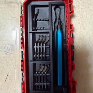 May include: A red plastic storage case with a clear hinged lid containing a black 3D-printed insert. The insert holds a blue metal deburring tool handle and several interchangeable black metal blades arranged in organised slots within the case.
