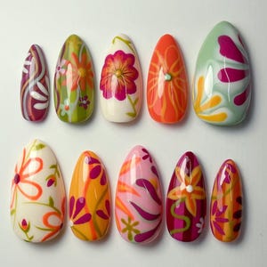 May include: A set of ten almond-shaped press-on nails featuring various floral and abstract patterns in vibrant colors including orange, pink, green, yellow, and white. Each nail has a glossy finish and distinct hand-painted designs.