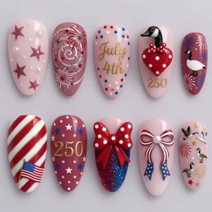 May include: A collection of ten artificial nails with various designs. The designs include fireworks, stars, the text "July 4th", a heart, a bow, and an American flag. The nails are painted in shades of pink, red, white, and blue.