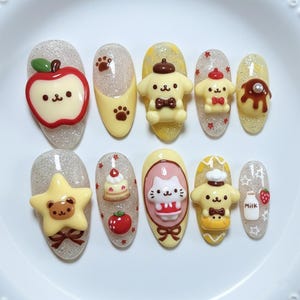 May include: A set of ten artificial nails with various 3D designs. The designs include an apple, paw prints, cartoon characters, a cake, a cat, a star, a strawberry, and a milk bottle. The nails have glitter and a variety of colors.