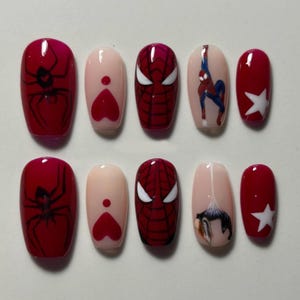 May include: A set of ten press-on nails featuring a red and nude color palette. Designs include black spider silhouettes, red hearts, a red and black spiderweb mask pattern, a superhero figure in blue and red, and white star accents.