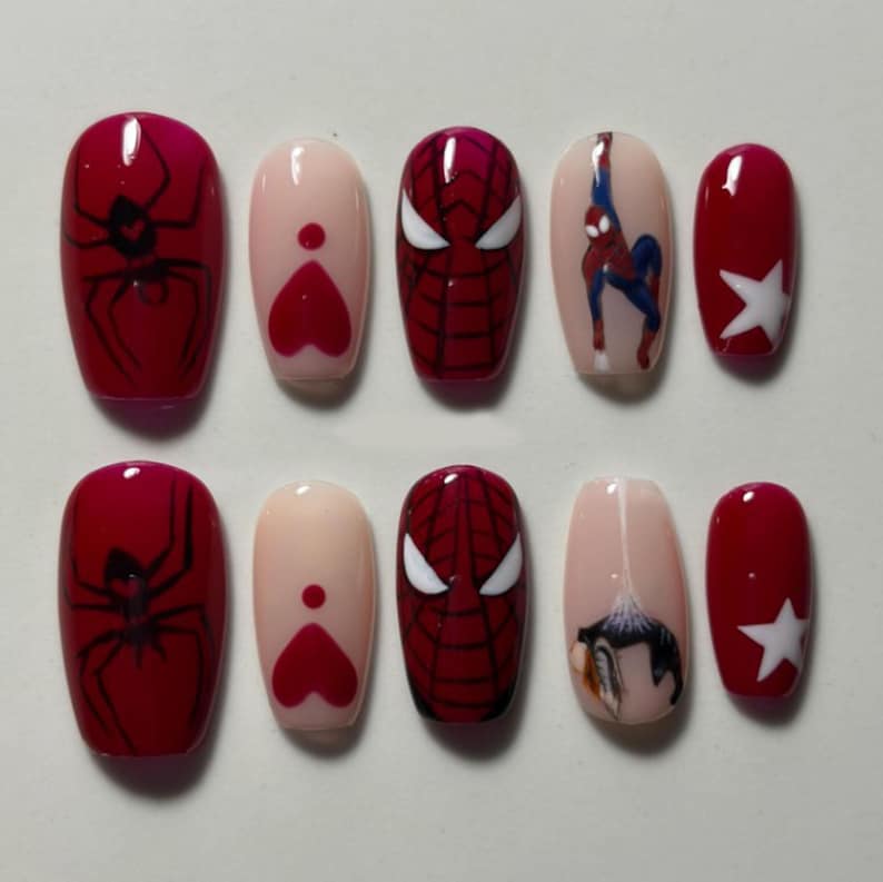 May include: A set of ten press-on nails featuring a red and nude color palette. Designs include black spider silhouettes, red hearts, a red and black spiderweb mask pattern, a superhero figure in blue and red, and white star accents.
