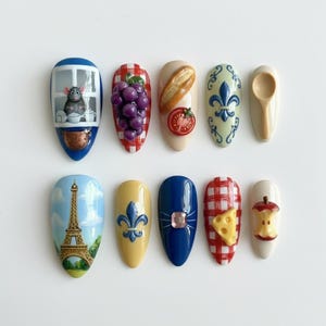 May include: A set of ten nail art designs featuring various themes. Designs include a rat in a window, grapes, a baguette with a tomato, a fleur-de-lis, a spoon, the Eiffel Tower, a jewel, cheese, and an apple.