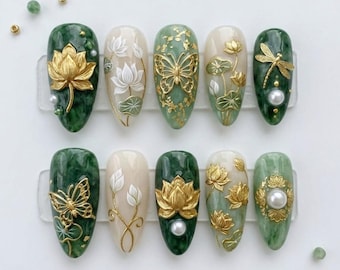 May include: A set of ten artificial nails with a jade green, cream, and gold color scheme. Each nail features intricate designs, including gold butterflies, lotus flowers, and dragonflies. Some nails have pearl accents.