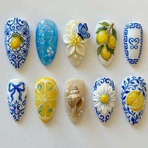 May include: A collection of ten artificial nails with various designs. The designs include lemons, butterflies, seashells, and floral patterns. The color palette features blue, yellow, white, and beige.