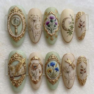 May include: A set of ten almond-shaped artificial nails with intricate designs. Each nail features a different design, including botanical illustrations, gold frames, and a dragonfly. The color palette includes soft greens, creams, and gold accents.