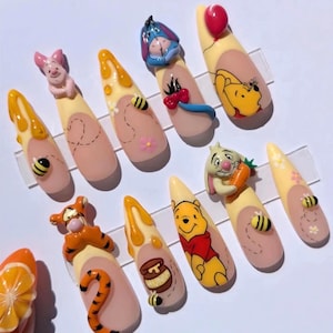 May include: A set of ten almond-shaped press-on nails featuring Winnie the Pooh characters including Piglet, Eeyore, Tigger, and Rabbit. The designs incorporate 3D elements like honey drips, bees, flowers, a carrot, and a red balloon on a nude base.