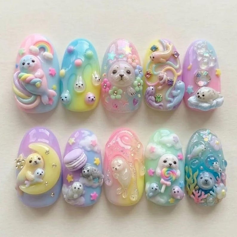 Op de afbeelding: Een set van tien kunstnagels, elk uniek ontworpen met pastelkleuren en 3D-versieringen. De ontwerpen tonen zeehonden, regenbogen, wolken en bloemen, wat een grillige en artistieke uitstraling cre&euml;ert. De nagels zijn ovaal van vorm en tonen een verscheidenheid aan texturen en details.