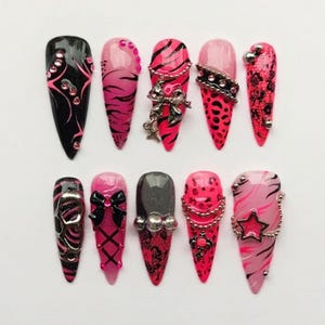 May include: A set of ten stiletto-shaped press-on nails featuring a black and hot pink color palette. The designs include zebra stripes, leopard spots, lace patterns, silver metallic charms, bows, stars, and embedded rhinestones on various nails.