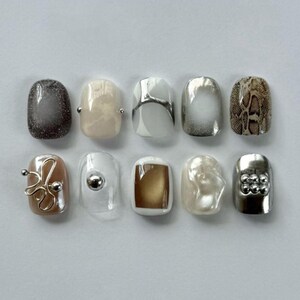 May include: A set of ten press-on nails featuring diverse designs including dark gray glitter, cream, white with silver lines, silver chrome, snakeskin print, a gold wire accent, a clear nail with a silver bead, a gold square, pearl, and silver studs.