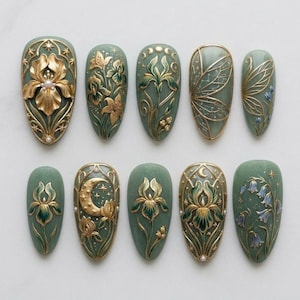 Könnte beinhalten: Ein Set aus zehn mandelförmigen, salbeigrünen Kunstnägeln. Jeder Nagel weist aufwendige gold- und grünfarbene Blumen- und Himmelsmotive auf, darunter Schwertlilien, Lilien und ein Mond. Einige Nägel haben einen Perlenakzent.