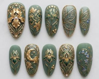 May include: A set of ten almond-shaped, sage green press-on nails. Each nail features intricate gold and green floral and celestial designs, including irises, lilies, and a crescent moon. Some nails have a pearl accent.