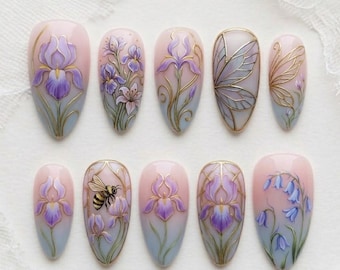 May include: A set of ten almond-shaped artificial nails. Each nail features a different floral design, including irises, butterflies, and bees, painted in shades of purple, blue, and gold on a pink and blue gradient background.