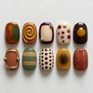 May include: A set of ten oval-shaped press-on nails featuring various designs including solid colours, stripes, polka dots, a spiral, a metallic frame, and glitter accents in shades of brown, cream, mustard yellow, olive green, and deep red.