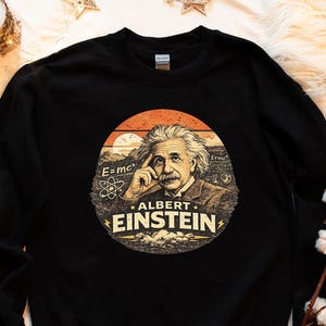 Puede incluir: Sudadera negra con un gráfico circular de Albert Einstein. El gráfico incluye la ecuación E=mc² y el texto "ALBERT EINSTEIN" sobre un fondo de puesta de sol. Diseño de estilo vintage.