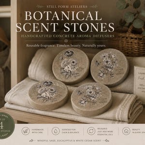 May include: A set of four round, beige concrete scent stones featuring black floral illustrations and text. Each stone displays botanical designs with phrases like Bloom Again and Bloom in Silence. The stones are arranged on folded fabric.