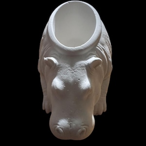 May include: A white ceramic hippopotamus planter with a large opening on its back. The planter is detailed with textured skin and facial features, set against a black background. The hippo is in a standing position.